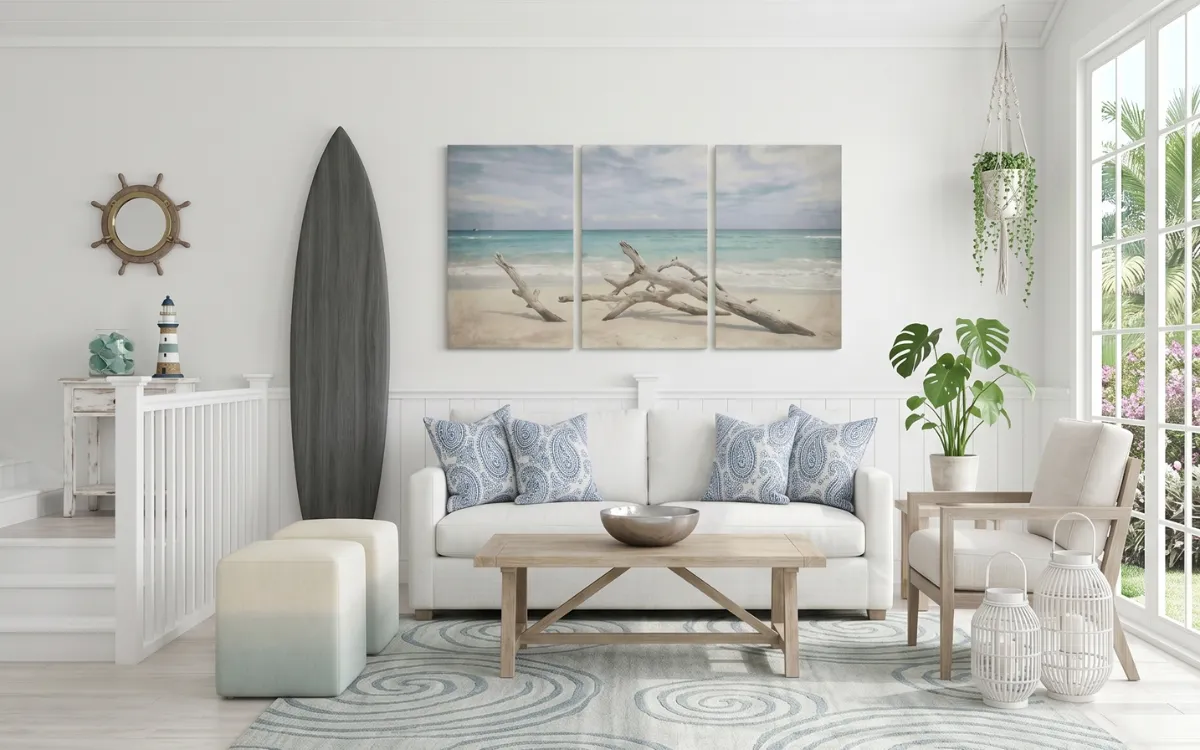 Bright coastal living room featuring a white sofa, decorative surfboard, triptych beach artwork, and blue paisley pillows.